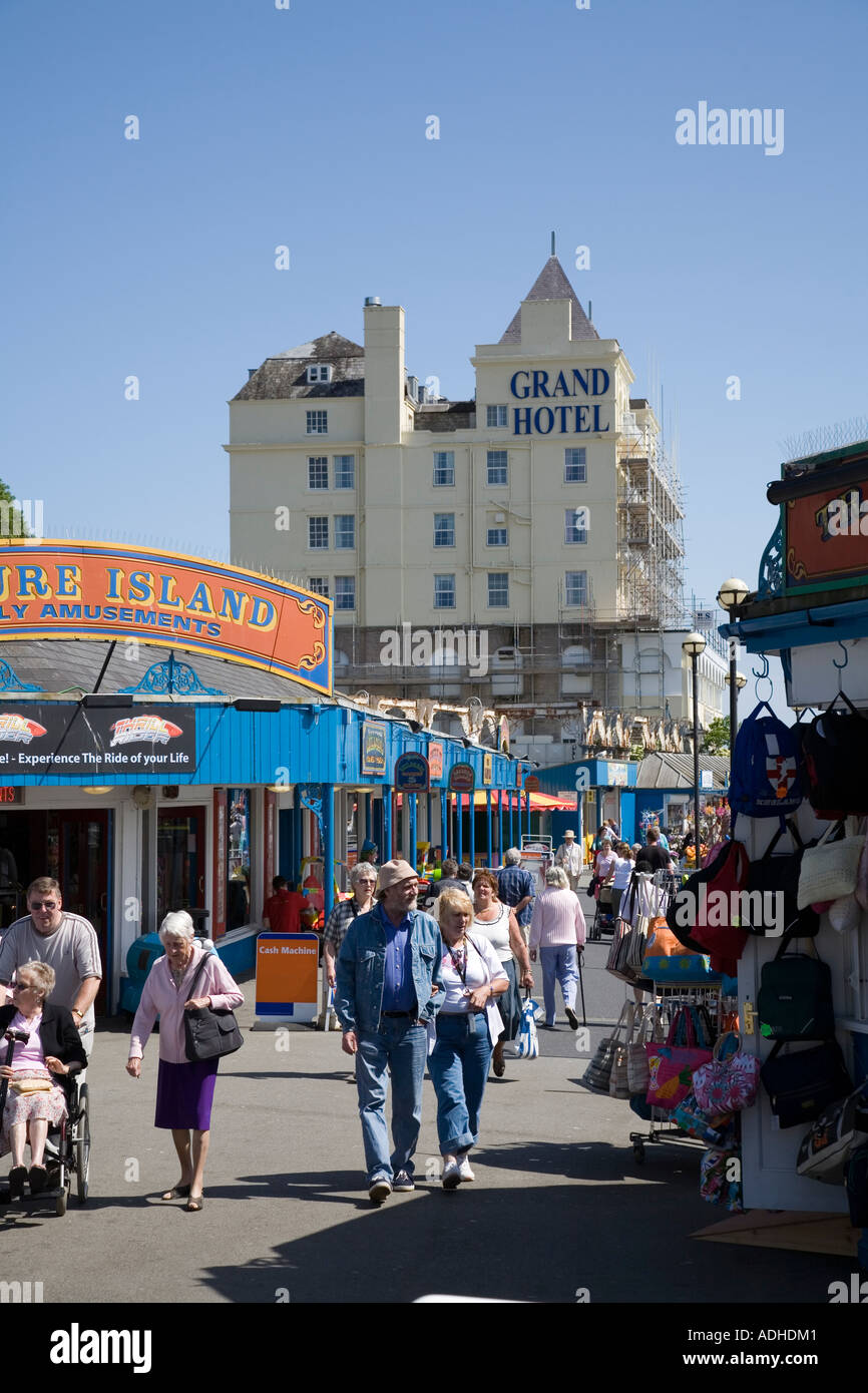 People walking on pier with amusement arcade and stalls in summer with Grand Hotel in background Llandudno Wales UK Stock Photo