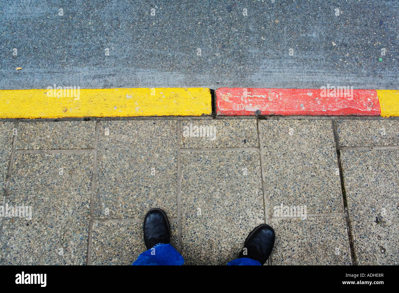 Feet and bus stop curb painted red and yellow Stock Photo
