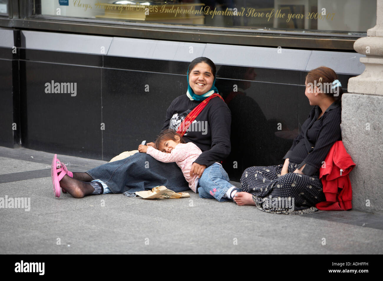 two gypsy beggar women with young girl sharing a joke whilst begging outside clearys on oconnell street dublin Stock Photo