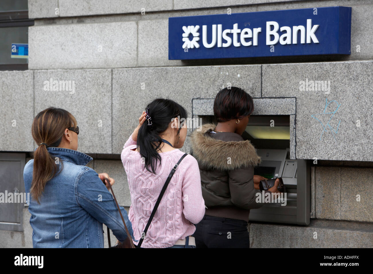 hispanic asian and black woman queue up at an ATM cash point ulster bank in oconnell street dublin Stock Photo