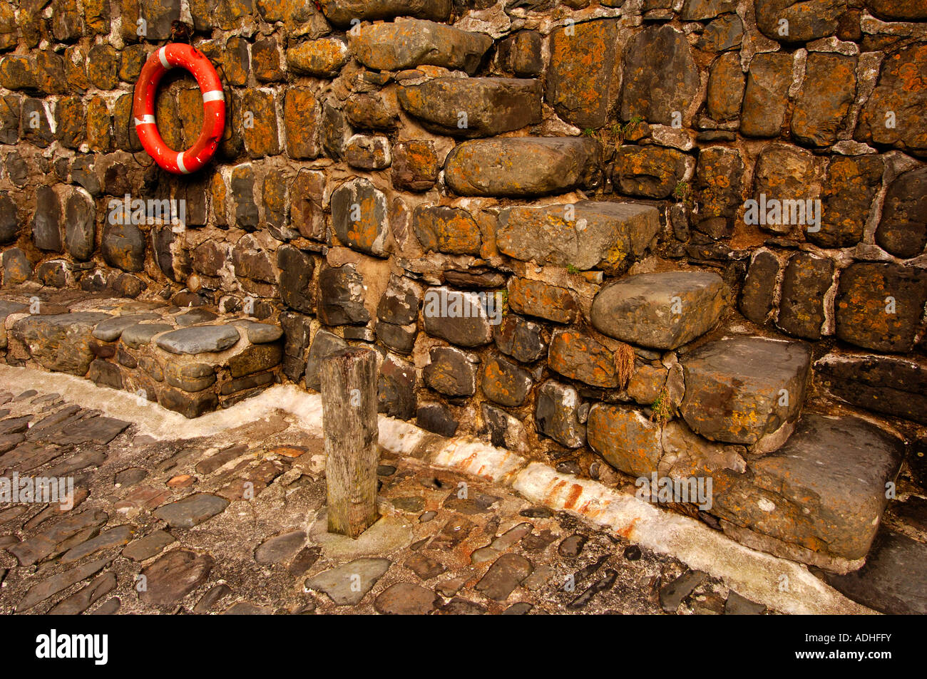 Ancient stone steps on the 14th century harbour wall at Clovelly with a bright orange modern life ring Stock Photo