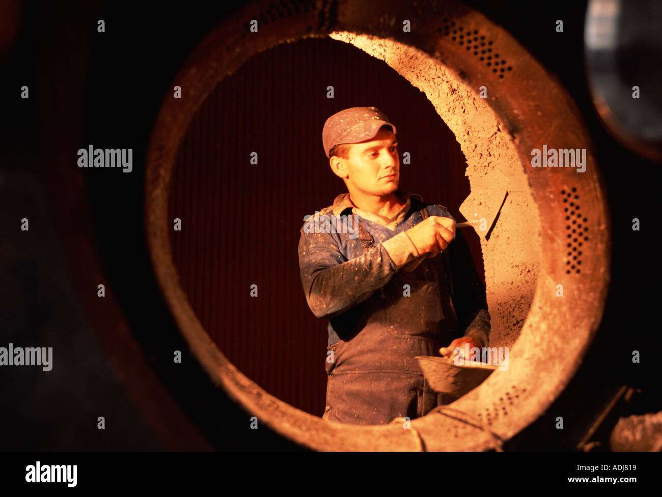 Belgrade, Serbia, Yugoslavia. Man working at an urban heating plant, using a trowel with fire cement inside a boiler. Stock Photo