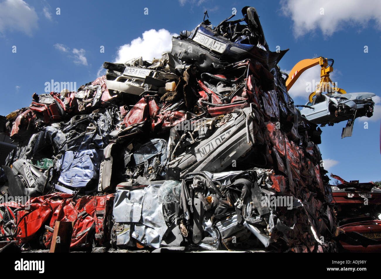Cubes of crushed cars stand in a huge pile as a crane lifts a Fiat Bravo into the crusher Stock Photo