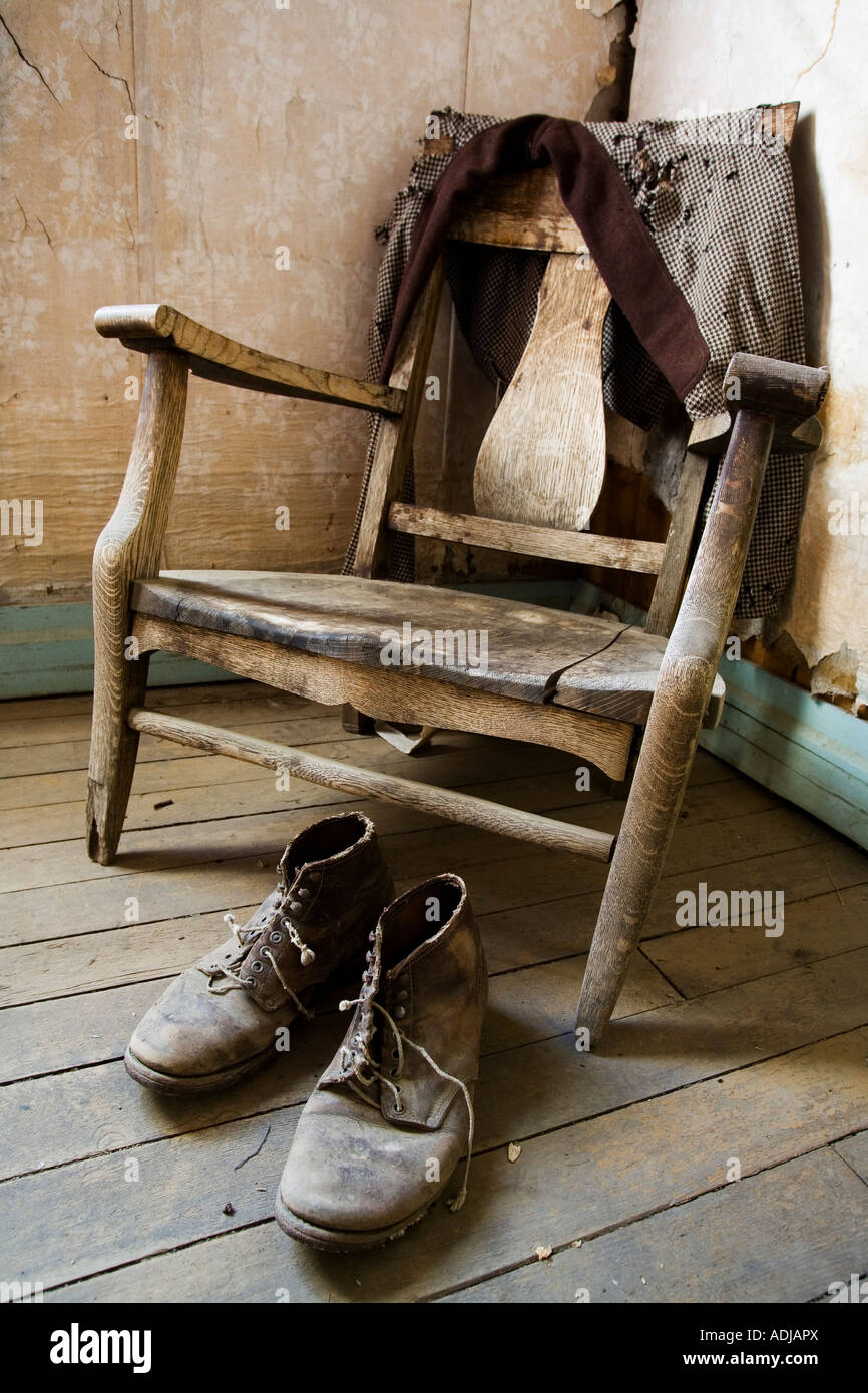 Old wooden chair a pair of work boots and a worn tattered jacket Stock Photo