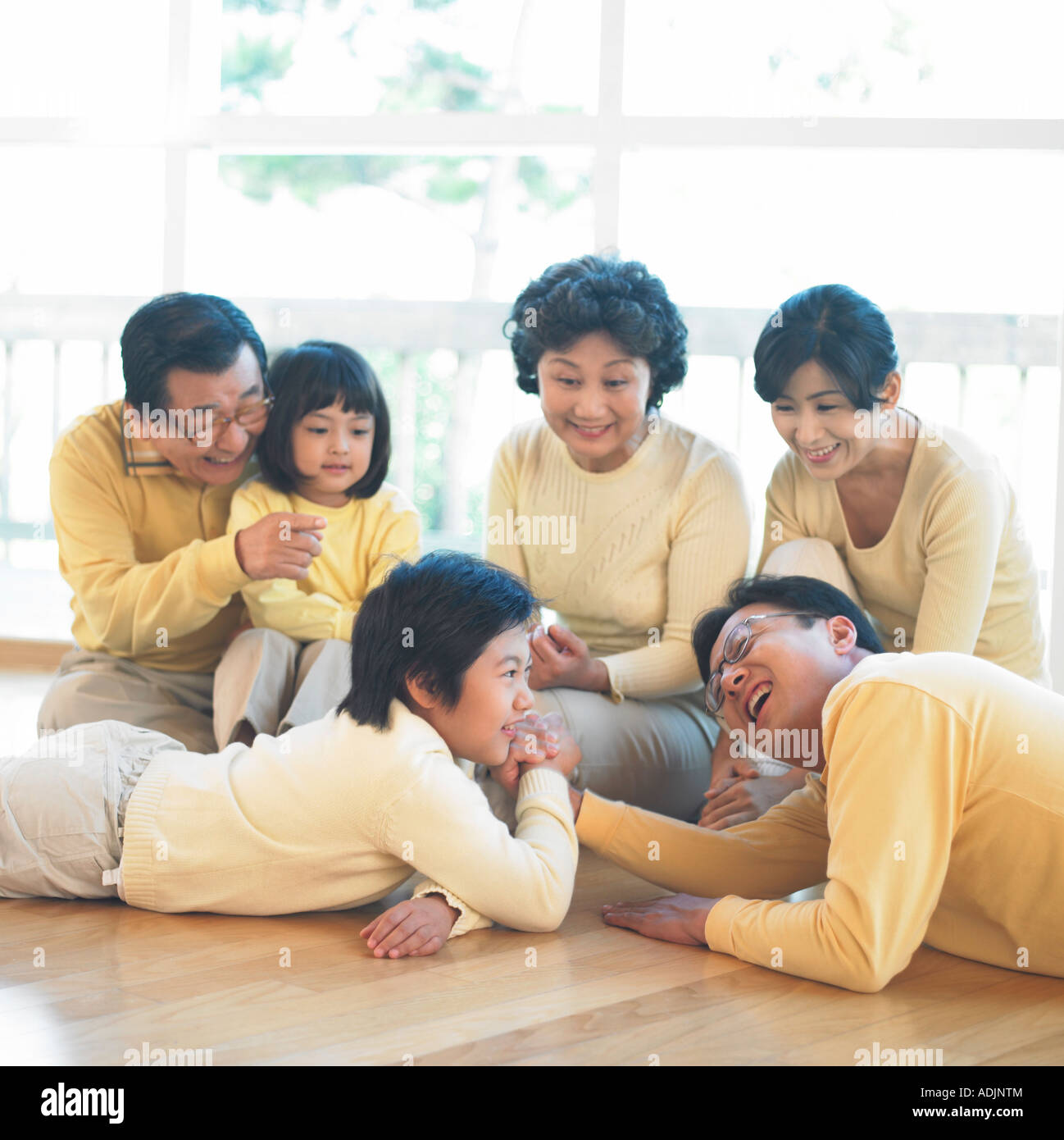 A Korean father and a son are doing an arm wrestling, and their family is looking at them Stock Photo