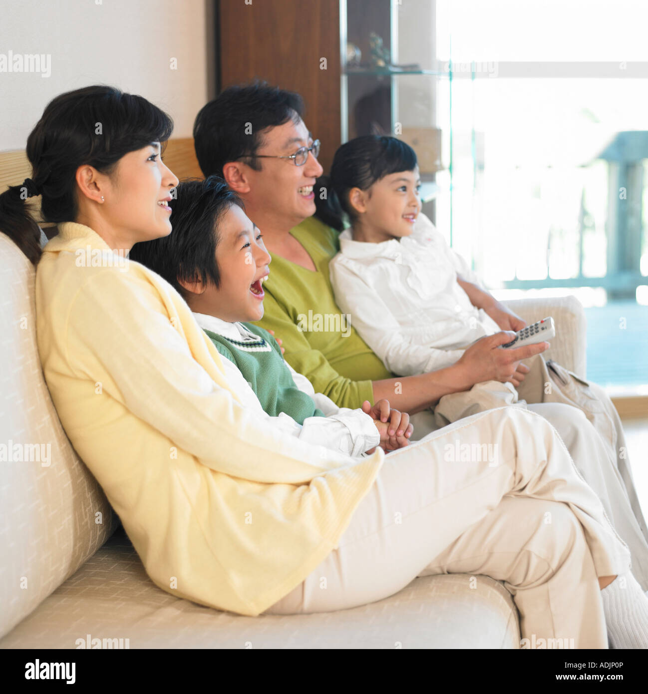 A Korean family is watching a TV and smiling in the living room Stock