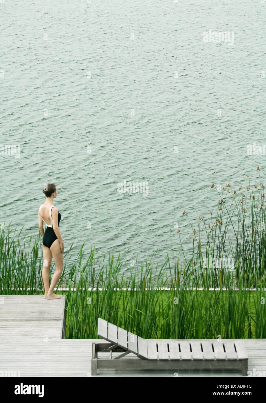 Woman in swimsuit standing on deck, looking towards body of water Stock Photo