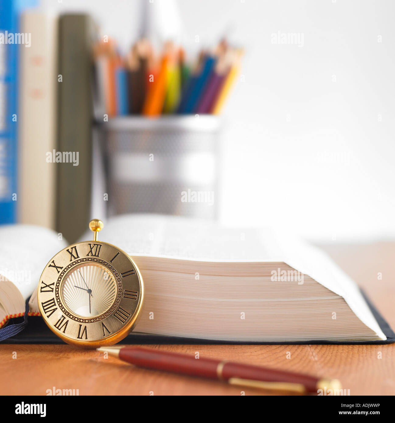 Notebooks, books, a pencil case, a clock, a pen and a opened dictionary
