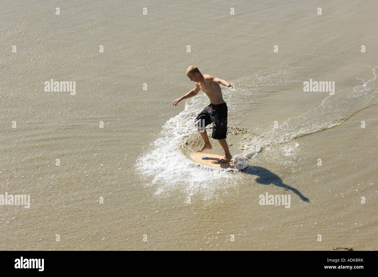 A skimboarder balances in motion at the California shoreline Stock Photo