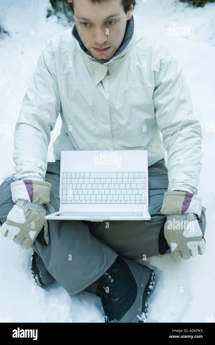 Young man sitting in snow, laptop on lap Stock Photo