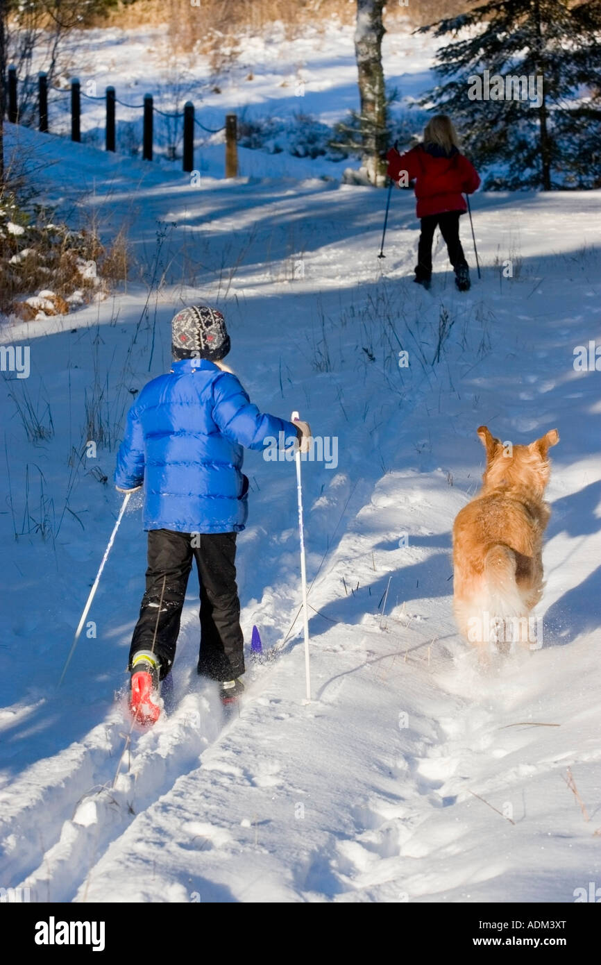 Two young girls cross country ski as golden retriever runs along with