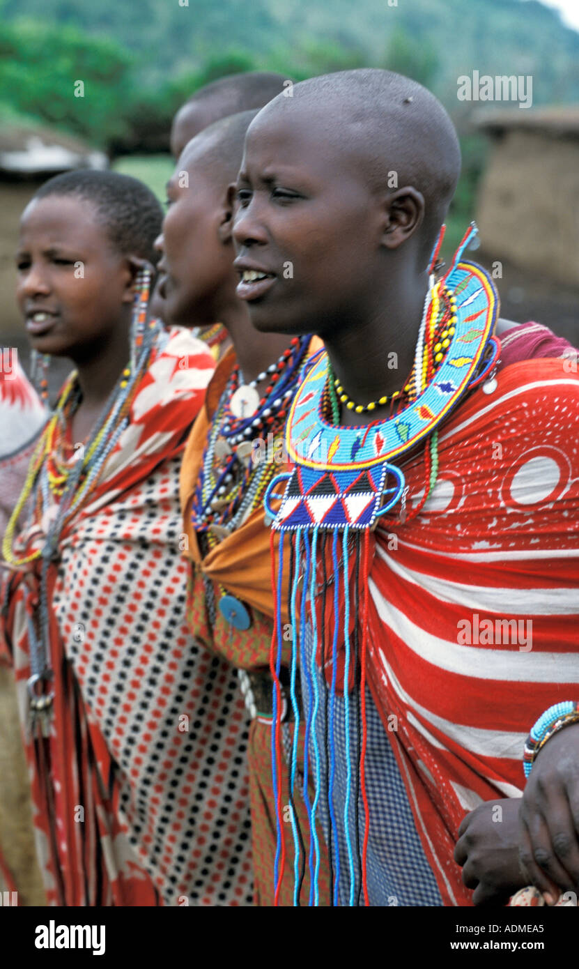 AFRICA KENYA Masai Mara National Reserve Young Masai women in traditional kanga cloth and beaded jewelry stand in their manyatta Stock Photo