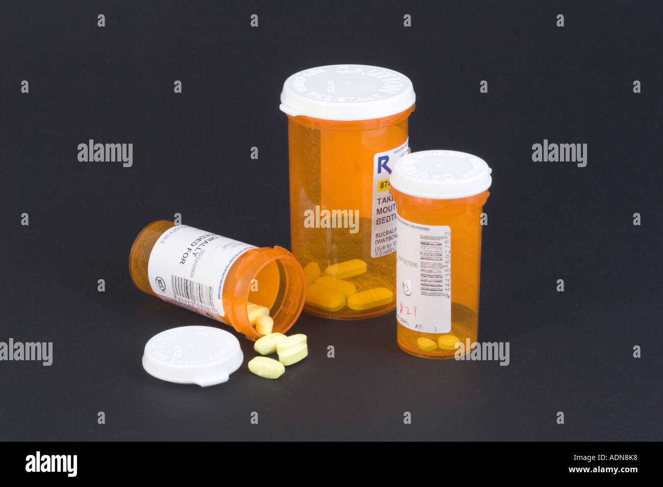Three medicine pill bottles on black background with open and closed bottles and pills spilling out Stock Photo