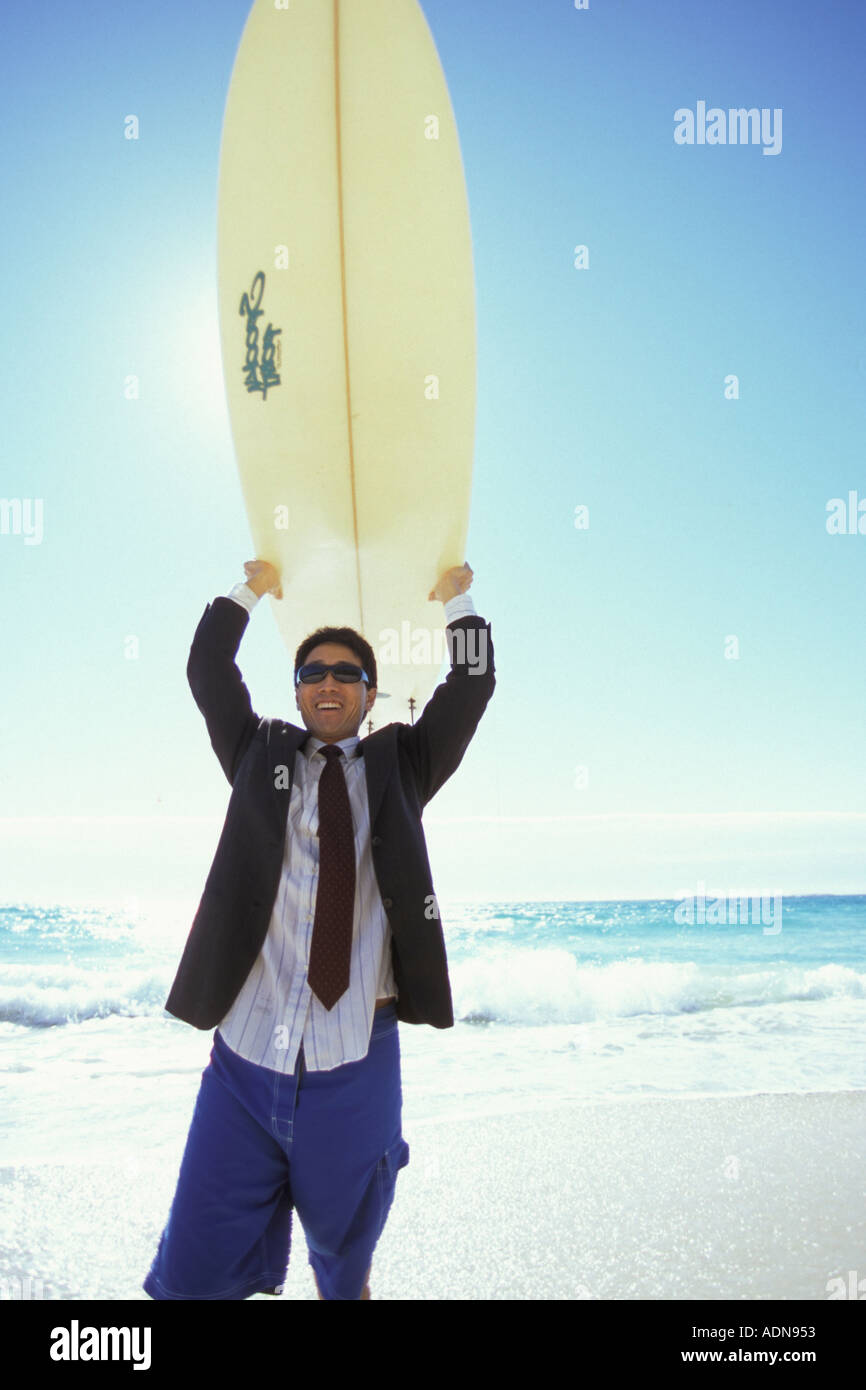 Businessman in jacket and shorts holding surfboard above his head Stock Photo