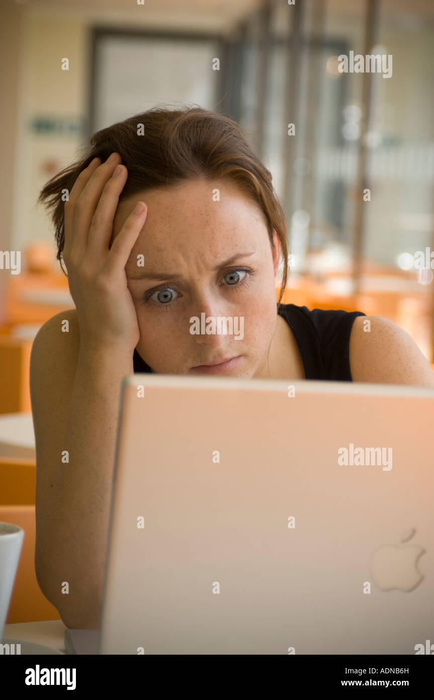 young red haired woman looking in disbelief at laptop computer in cafe bar checking email surfing web Stock Photo