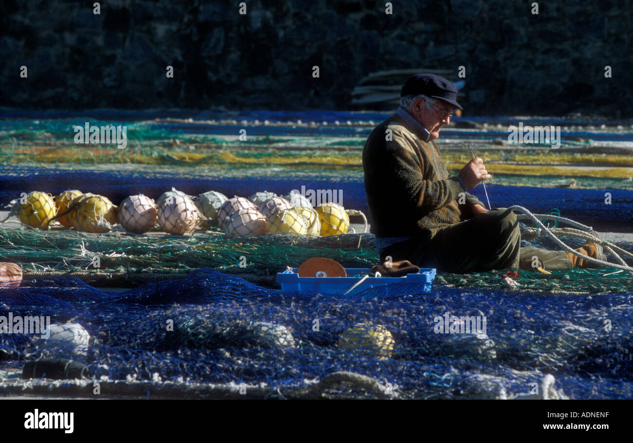 A fisherman repairs fishing nets in the harbour of Roses, Costa Brava, Spain Stock Photo