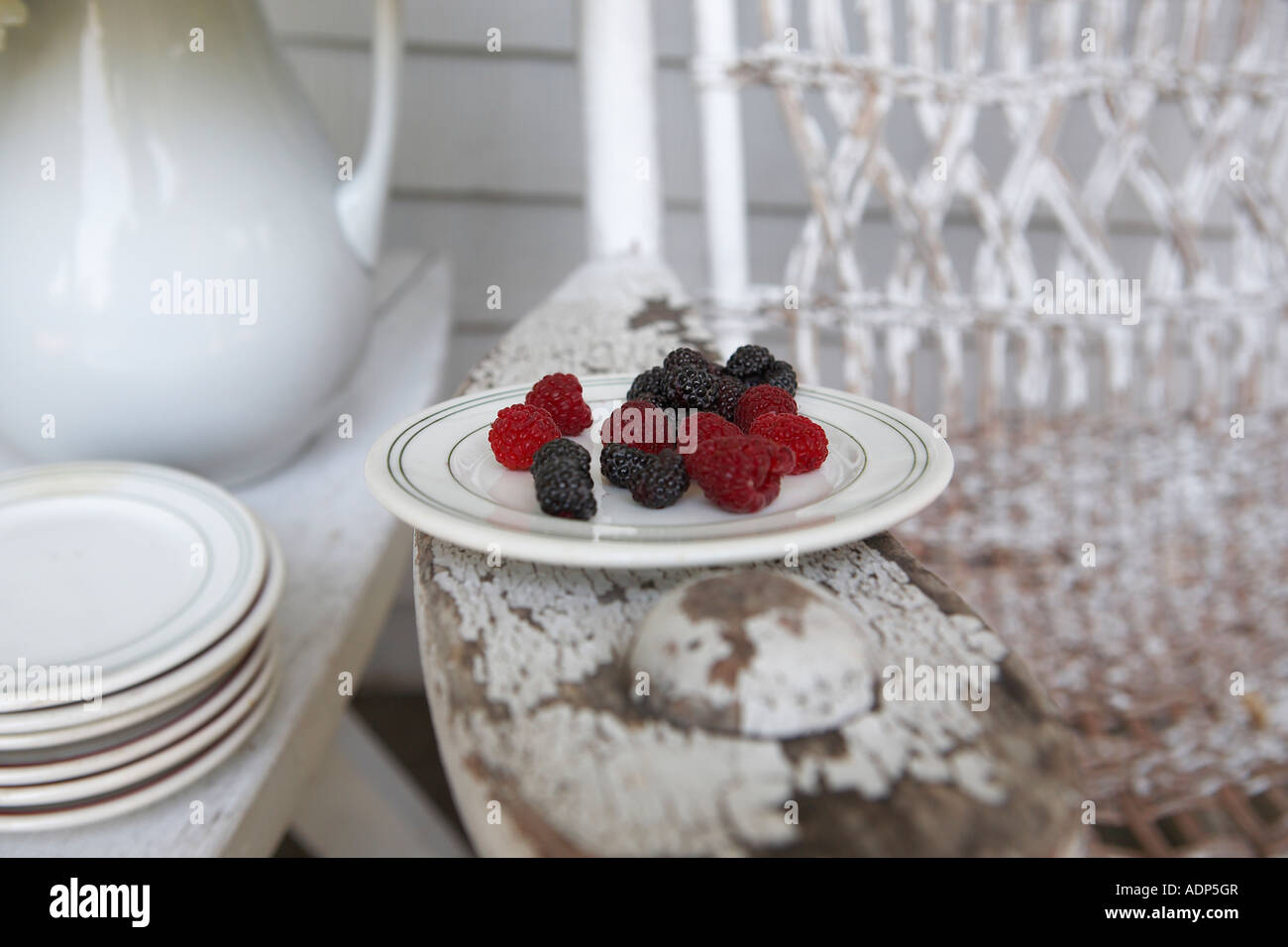 Plate of red and black raspberries set on the arm of an old rocking chair on the front porch Stock Photo