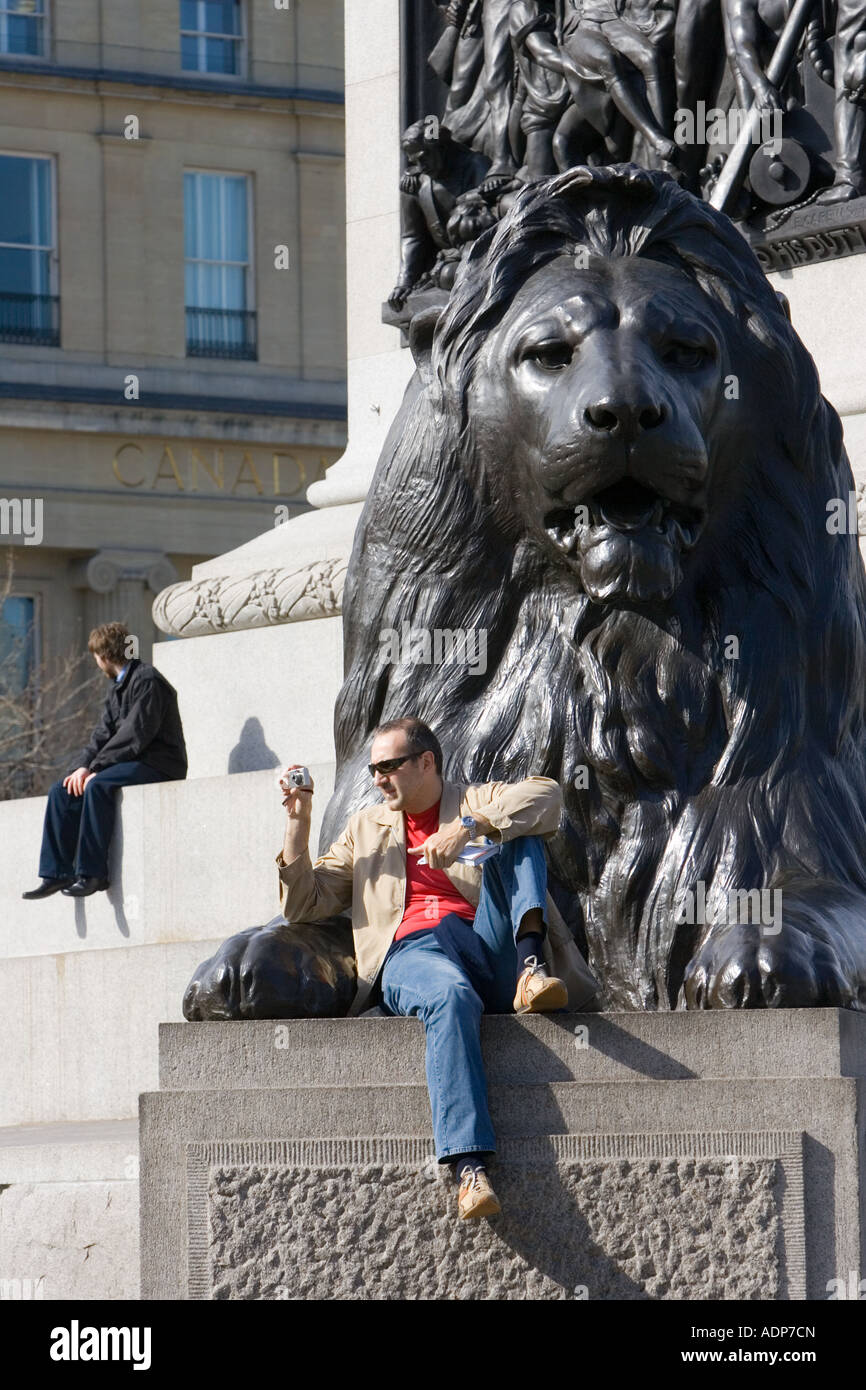 Tourist sits taking photographs on lion statues at base of Nelson s Column Trafalgar Square London UK Stock Photo