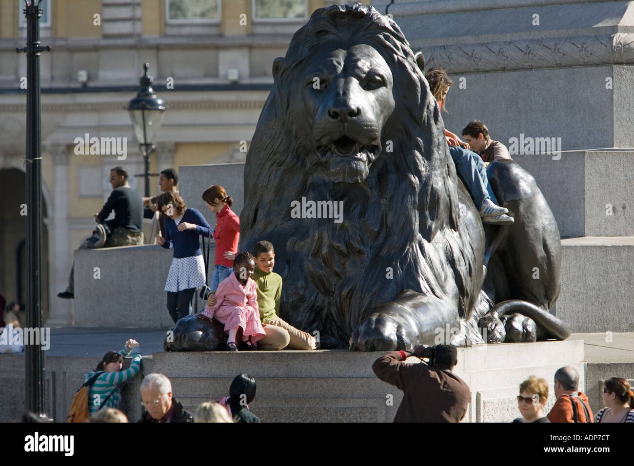 Tourists pose for photographs on lion statue at base of Nelson s Column Trafalgar Square London UK Stock Photo