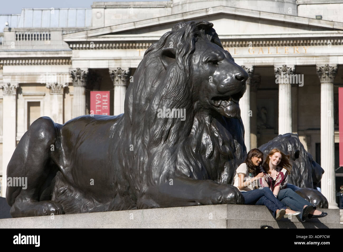 Tourists sit on lion statues in front of National Gallery in Trafalgar Square London United Kingdom Stock Photo