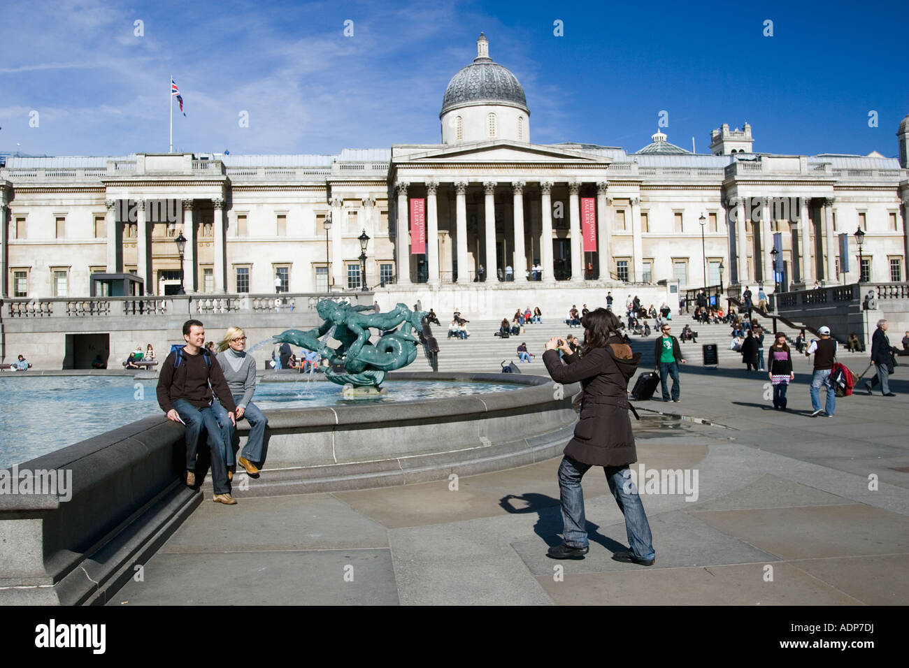 Tourists pose for photographs in Trafalgar Square by National Gallery London United Kingdom Stock Photo