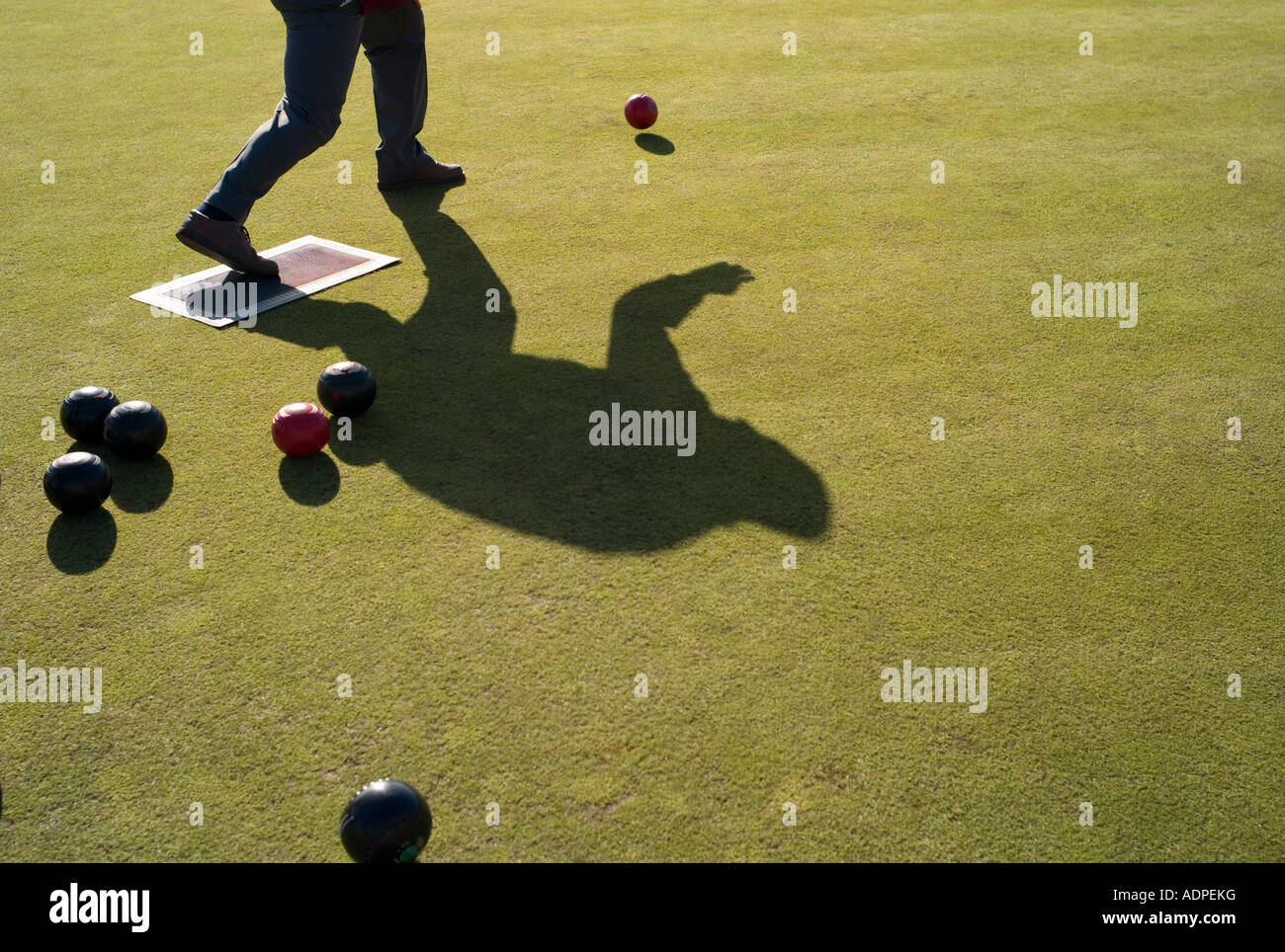 shadow of man playing outdoor bowls or bowling  on grass lawn in summer Stock Photo