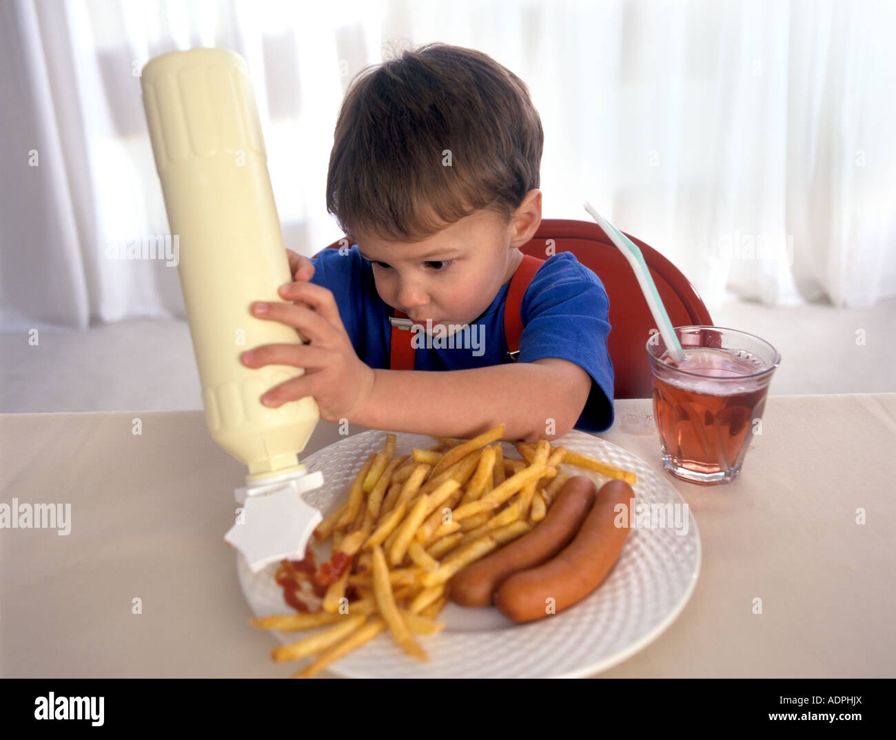 Little boy is putting a lot of ketchup on his dish of french fries and