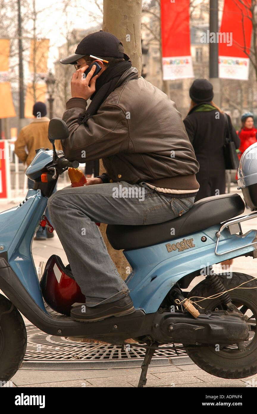 cigarette behind the ear Man on motor scooter with cigarette behind ear talking on cell phone on  Champs Elysees in Paris France Stock Photo