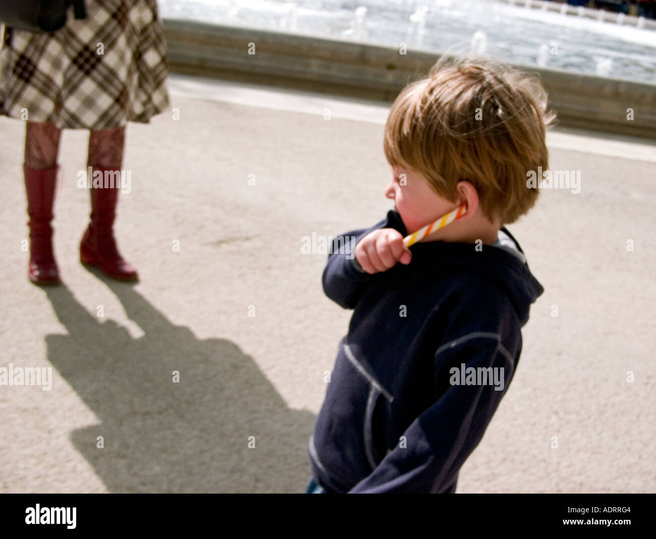 a little boy plays with a candy stick and his ear whilst his  mother watches on Stock Photo