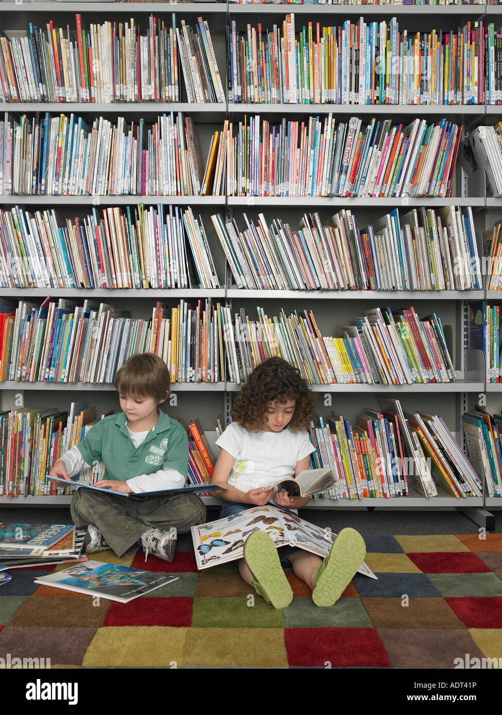 Boy and girl sitting on library floor reading books Stock Photo - Alamy