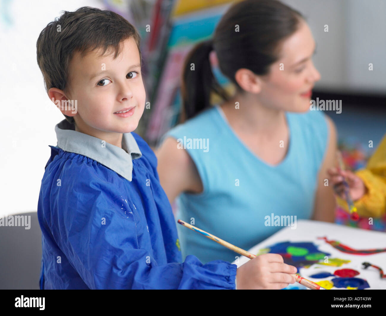 Art teacher squatting next to boy painting in art class Stock Photo Alamy