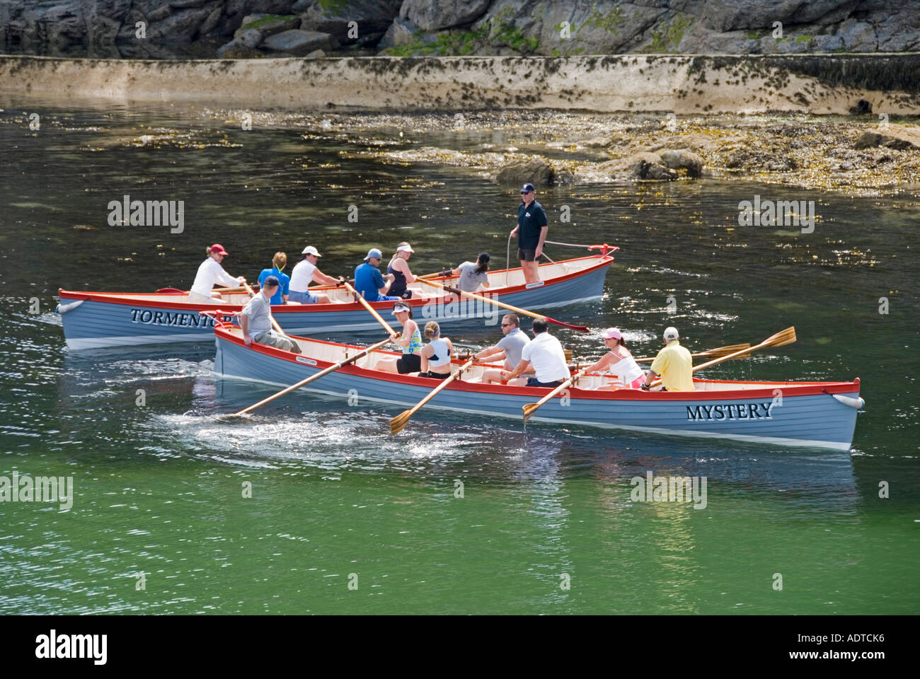 Charlestown waterfront mixed crew rowers two of a kind long pilot gig row boats prepare to race out to sea & back near St Austell Cornwall England UK Stock Photo