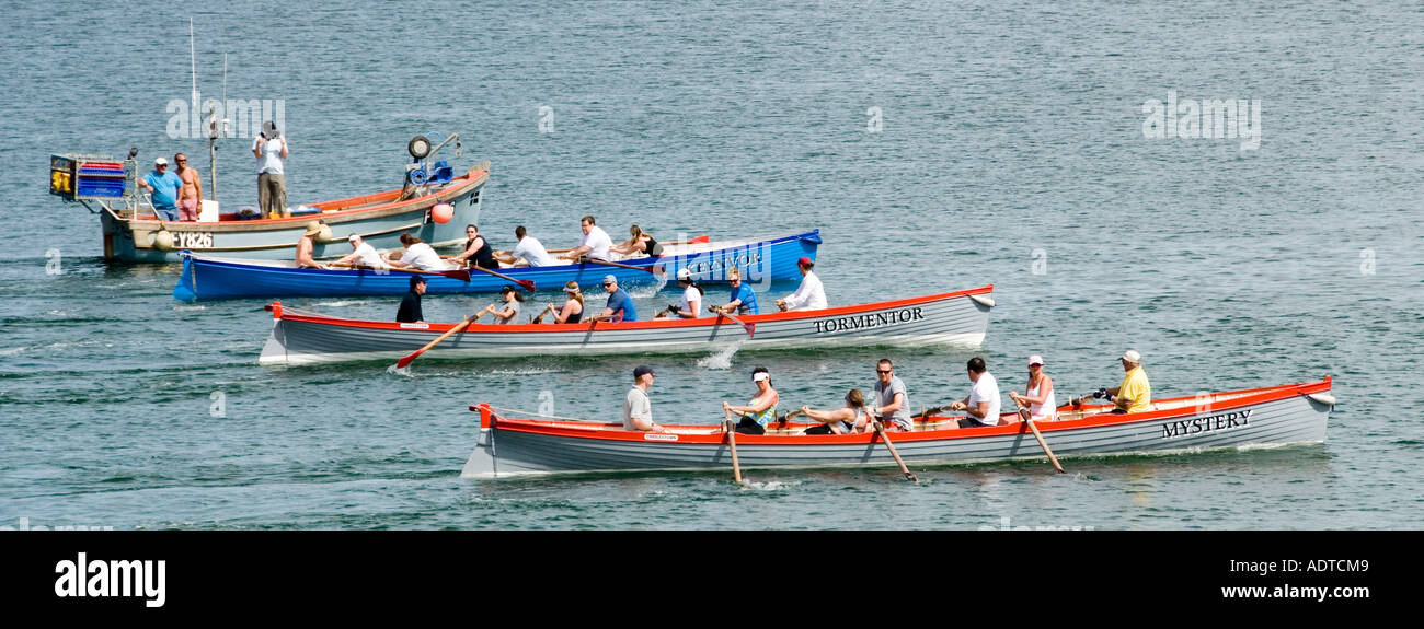 Off Charlestown shoreline mixed crew rowers in three teams long pilot gig row boats under starters orders race out to sea & back Cornwall England UK Stock Photo
