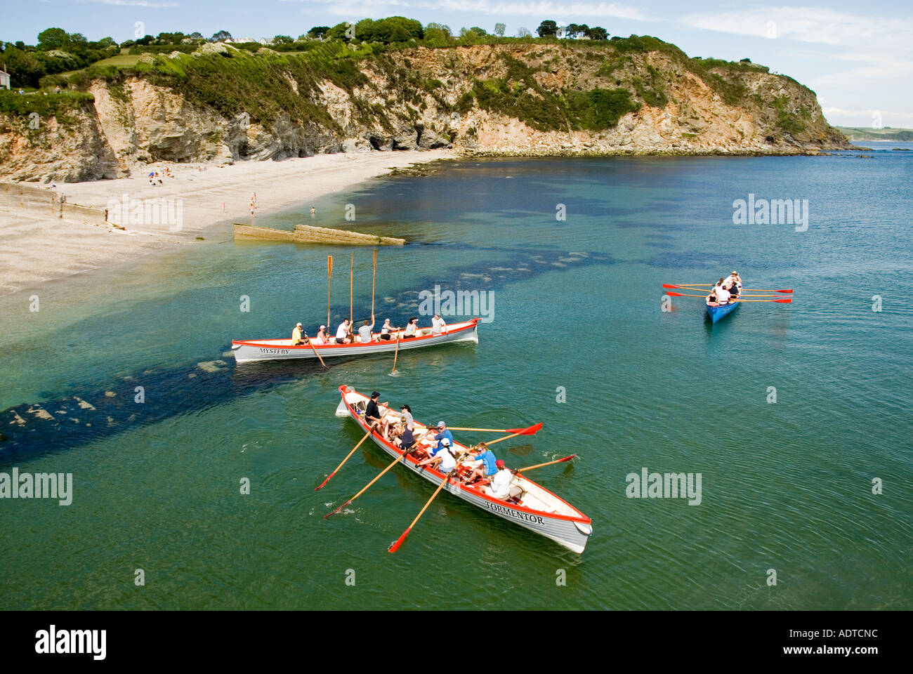 Winners hold oars aloft three mixed teams of long pilot gig row boats return to Charlestown shoreline after race out to sea & back Cornwall England UK Stock Photo