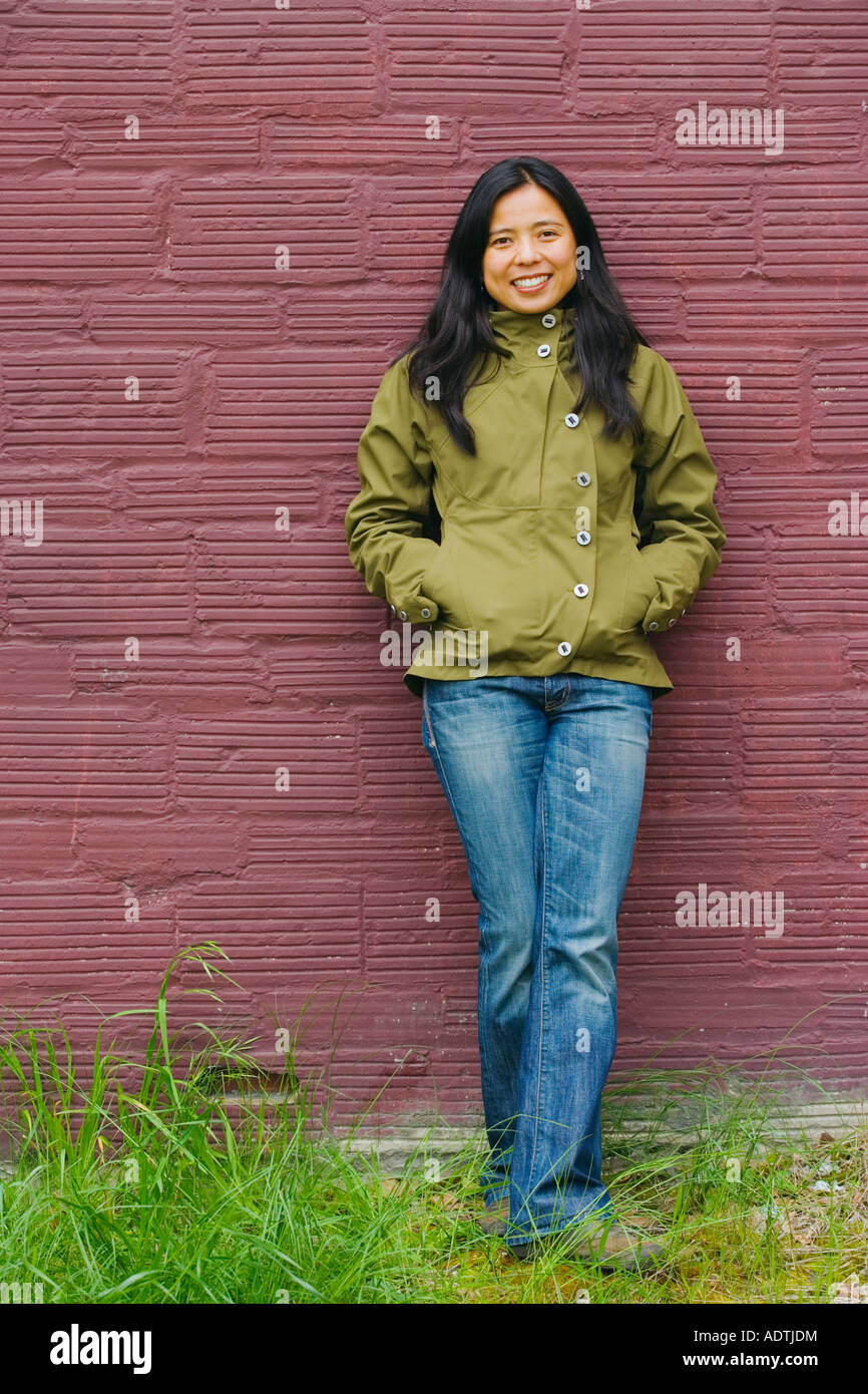 Portrait of smiling young woman leaning against maroon wall Stock Photo