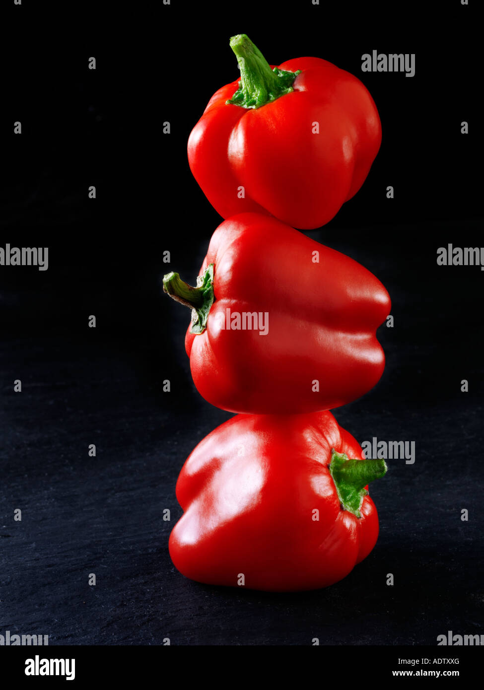 3 red peppers balanced on top of each other against a black background Stock Photo