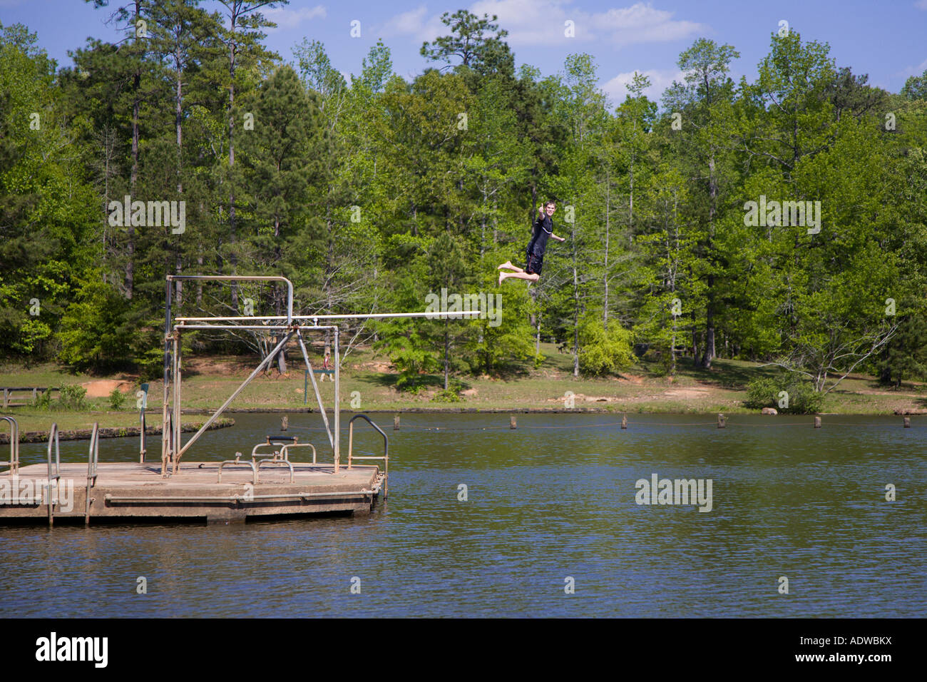 Teenage boy jumping from high diving board into lake giving thumbs up ...