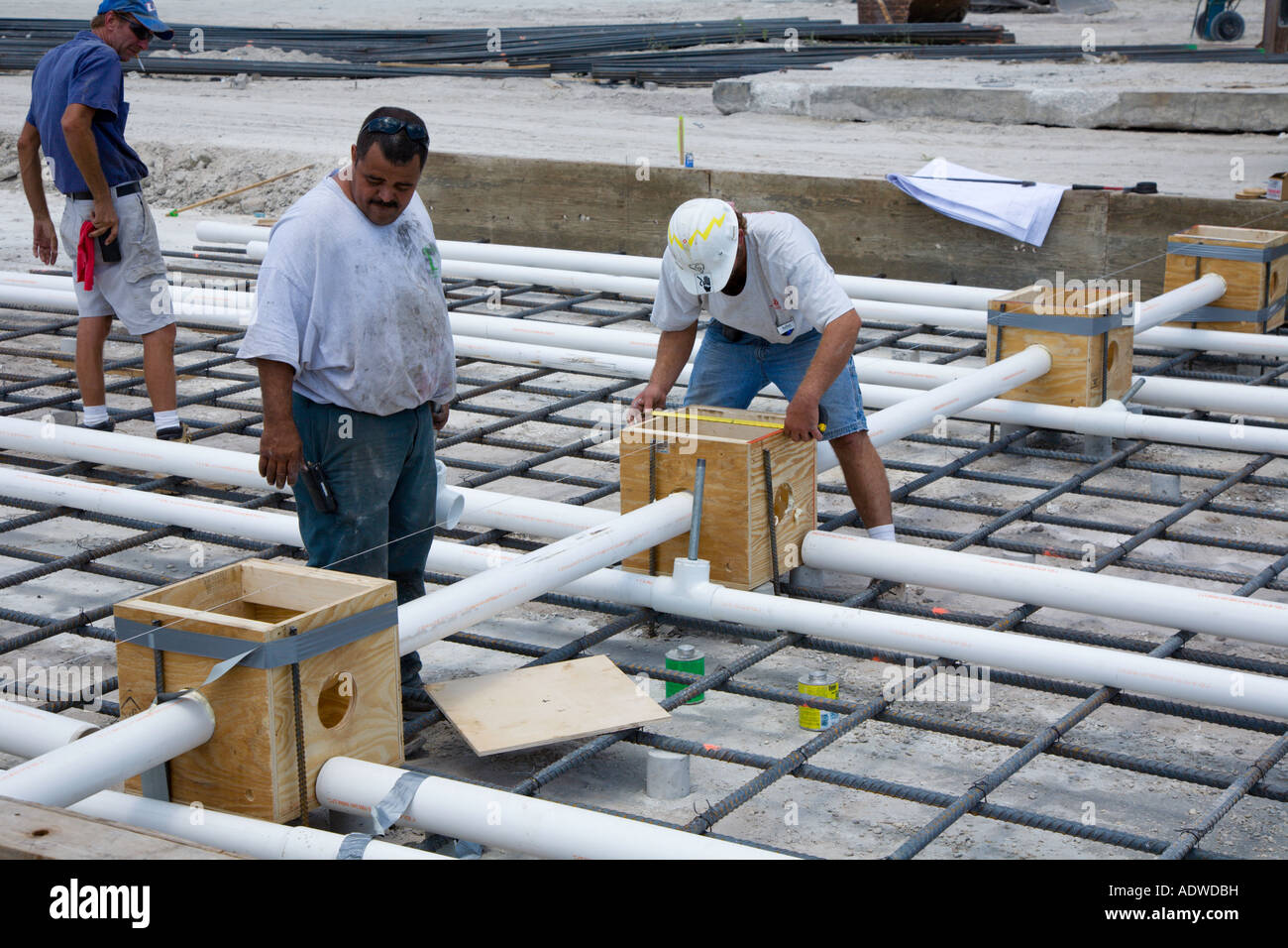 Three laborers placing formwork around rebar and PVC tied together on