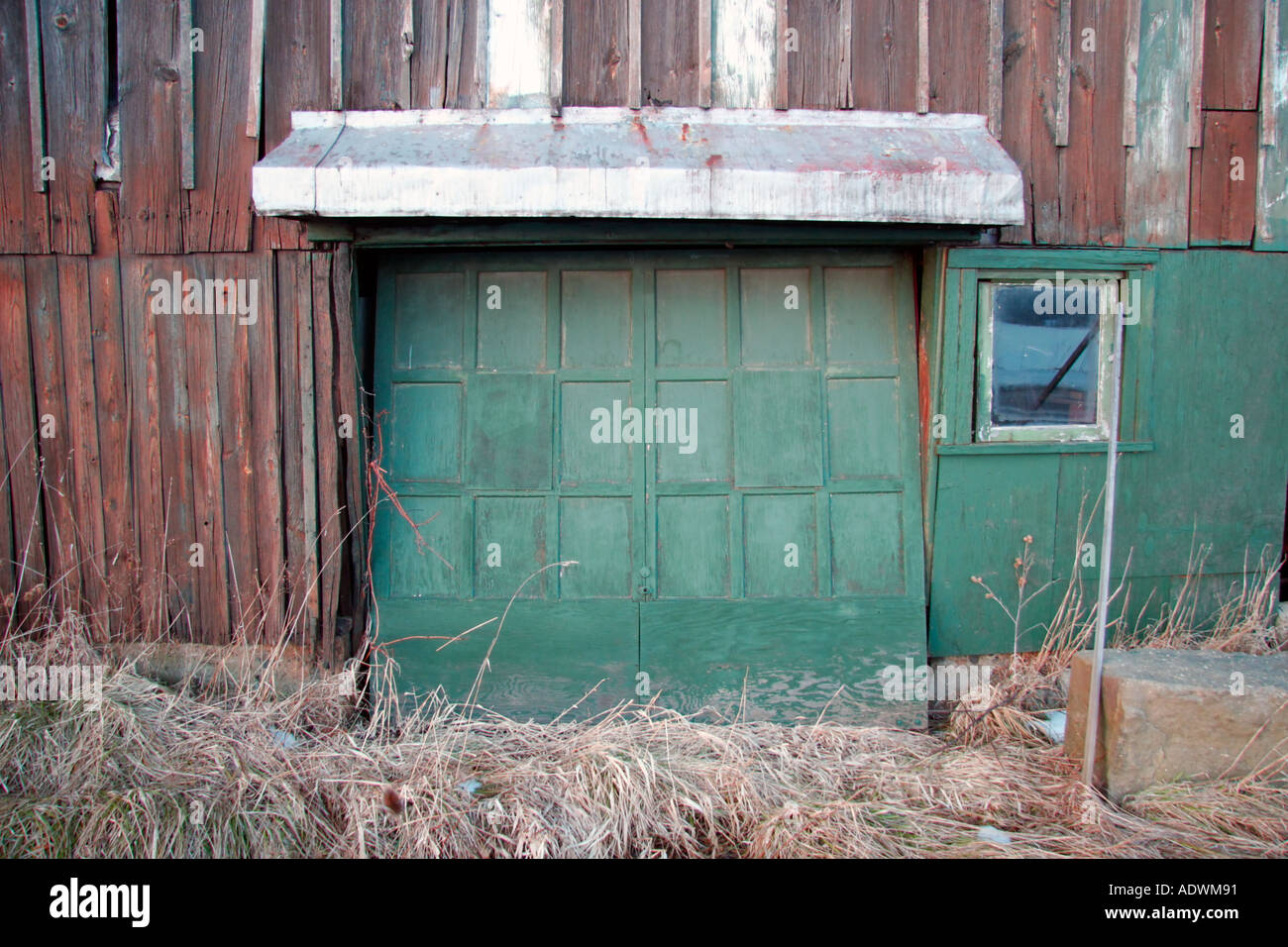 A Green Garage Door Is Slightly Open On A Brown Barn Over The Door
