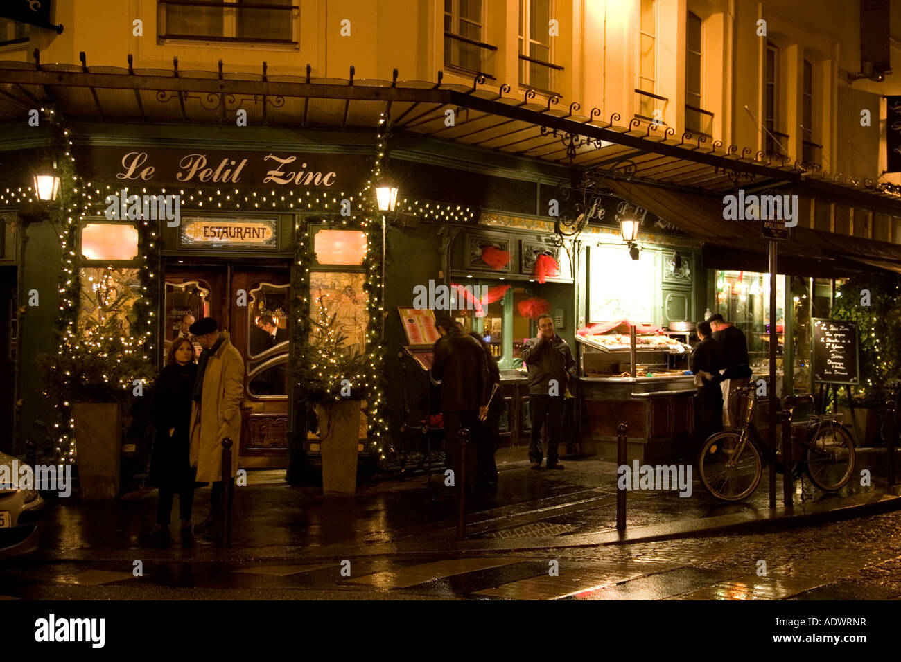 People shelter from rain at night on street corner outside traditional Le Petit Zinc Restaurant Left Bank Paris France Stock Photo