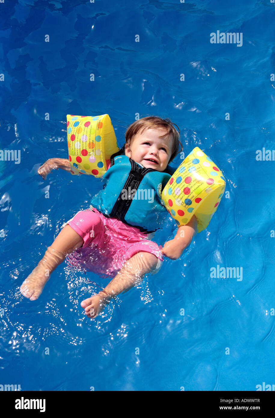 Baby girl floating on top of swimming pool in flotation jacket and arm