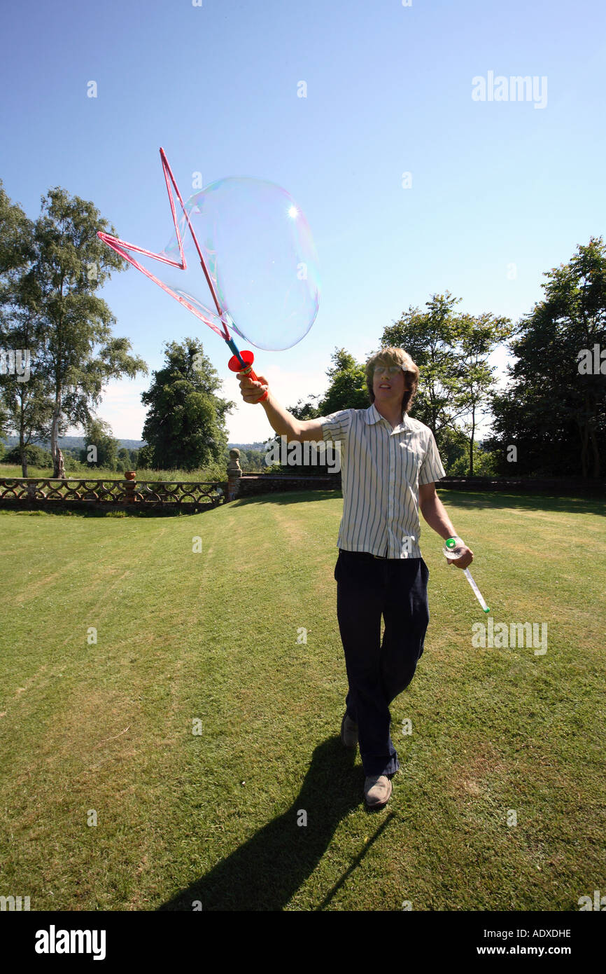 Man in mid twenty's blowing large bubbles outside using a bubble wand. Stock Photo