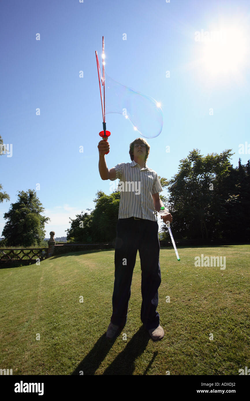Man in mid twenty's blowing large bubbles outside using a bubble wand. Stock Photo