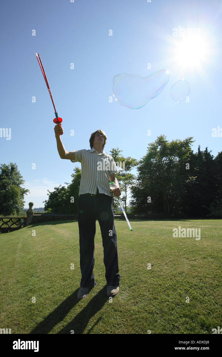 Man in mid twenty's blowing large bubbles outside using a bubble wand. Stock Photo