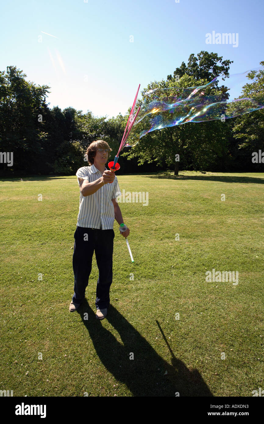 Man in mid twenty's blowing large bubbles outside using a bubble wand. Stock Photo