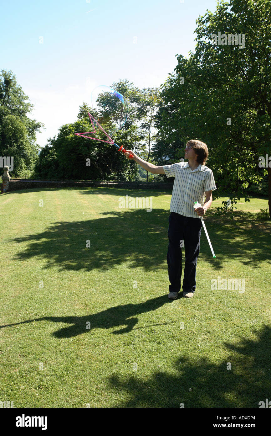 Man in mid twenty's blowing large bubbles outside using a bubble wand. Stock Photo