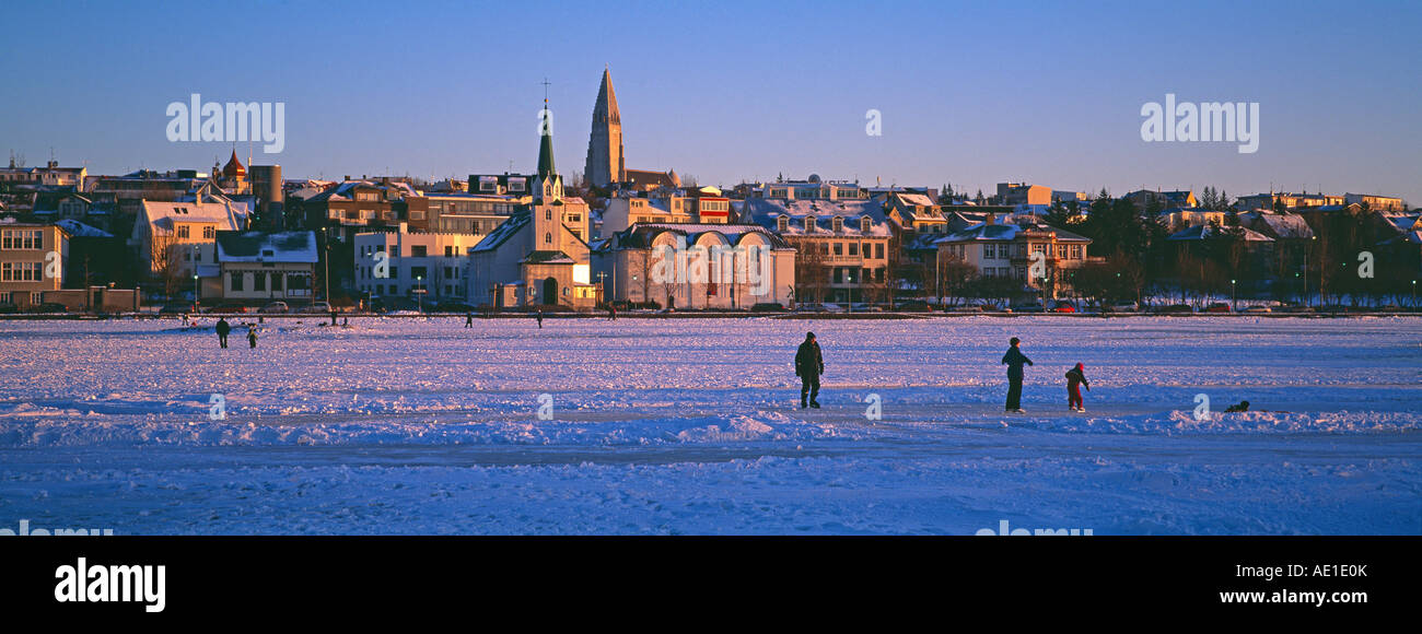 Iceland Reykjavik lake Tjorn frozen in winter local people skating and walking on the ice Frikirkjan church and Hallgrimskirkja Stock Photo