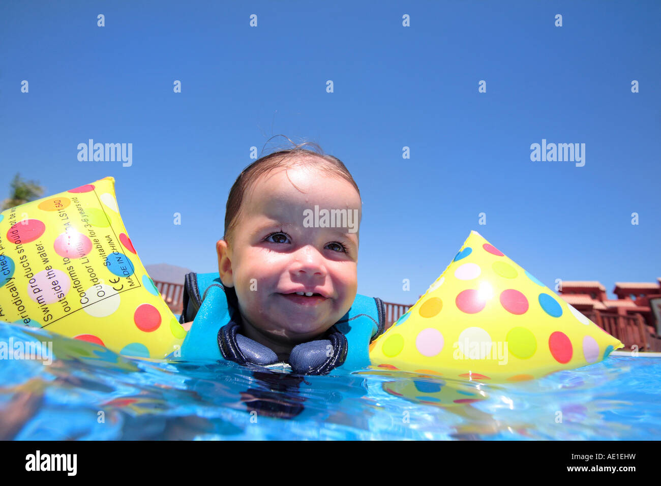 Baby girl floating on top of swimming pool in flotation jacket and arm