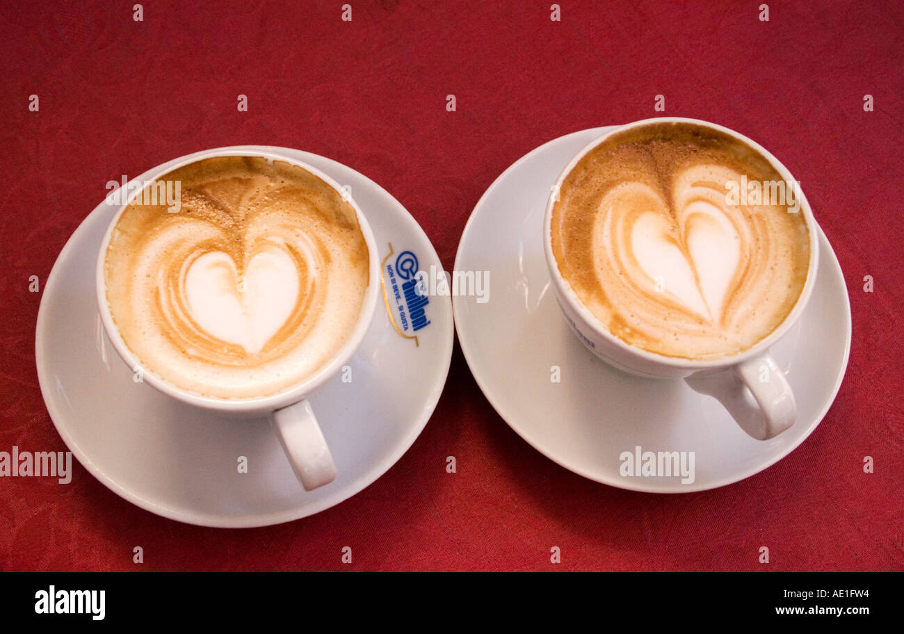 Two red cups of coffee on wooden background with latte art. Table in cafe.  Concept of easy breakfast. Small and big ceramic cups Stock Photo