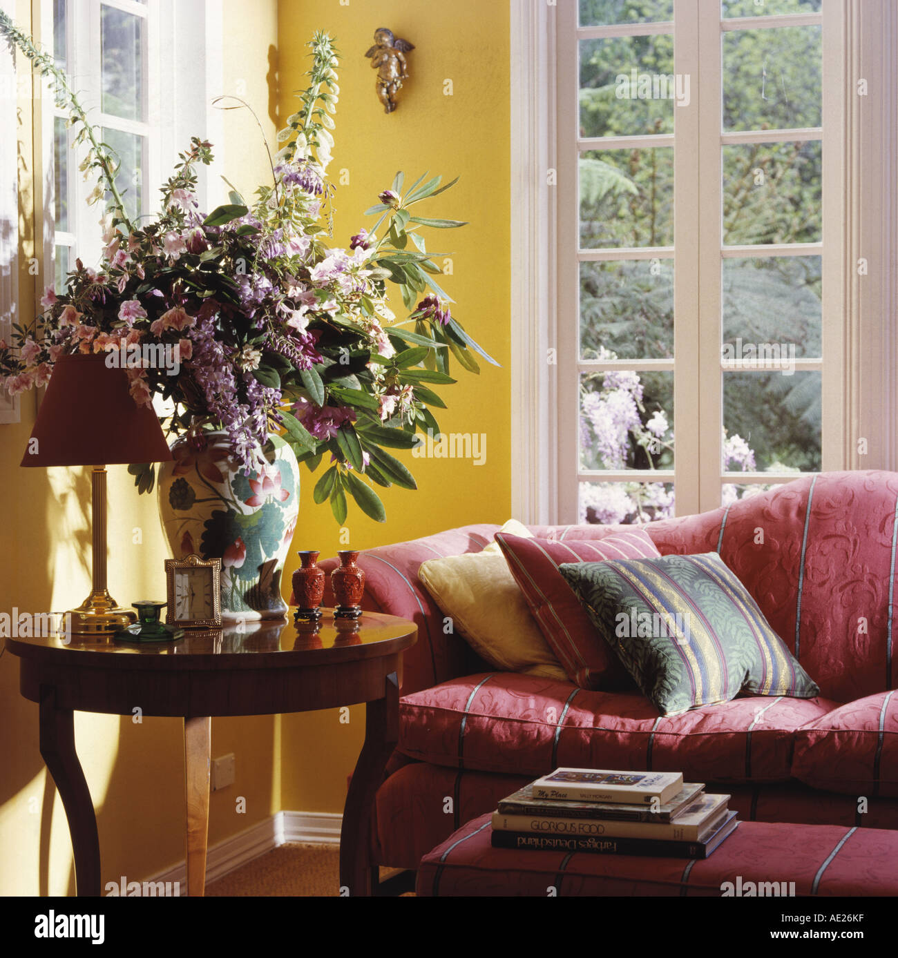 Vase of summer flowers on antique table beside pink sofa in front of French  windows in yellow living room Stock Photo - Alamy